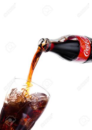 LONDON, UK - JANUARY 20, 2018: Pouring Coca Cola soda drink from bottle to glass on white. The drink is produced and manufactured by The Coca-Cola Company.